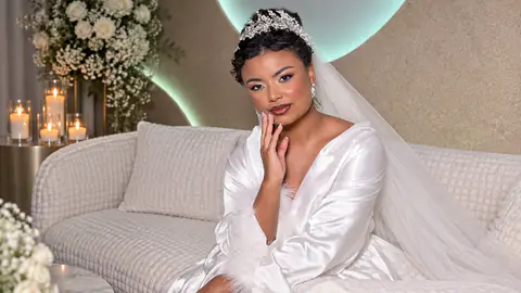 Noiva com tiara e véu sentada no sofá do estúdio, entre velas